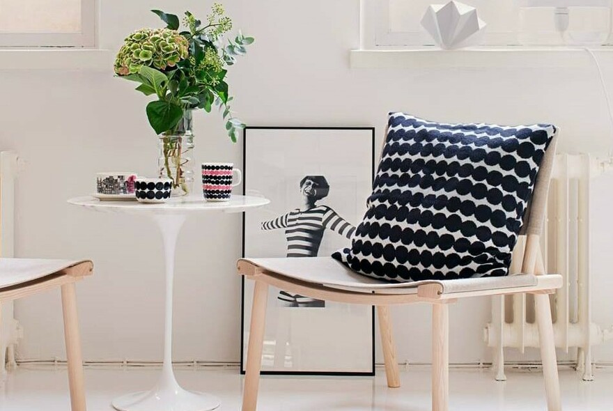 Hydrangea flower and green leaves in a glass vase on a small table. A cushion and black and white print are also in the room