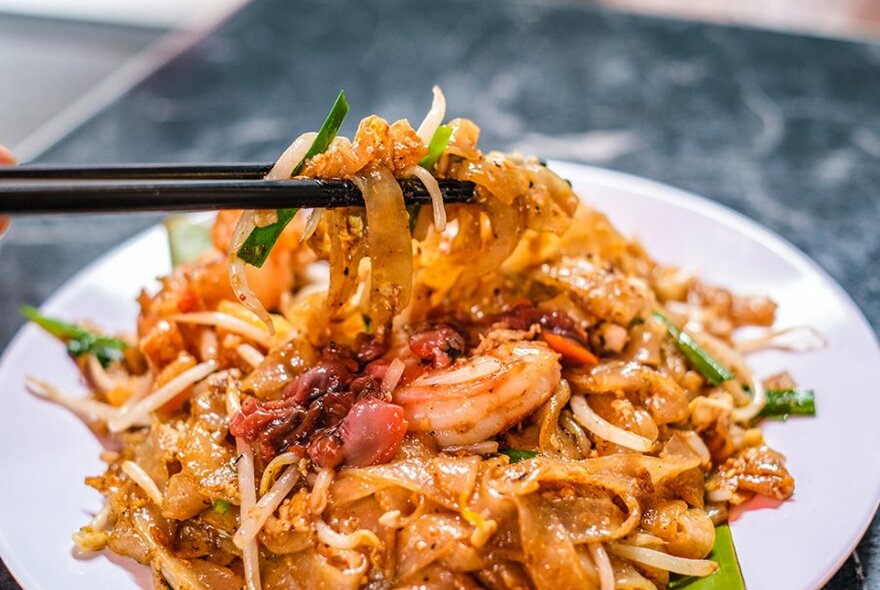 Chopsticks lifting noodles off a Malaysian dish.