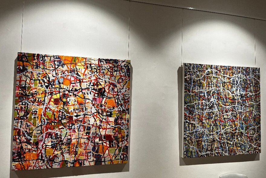 A spot-lit gallery wall showing two works by artist Matthew Simpson, both a tangle of coloured lines. 