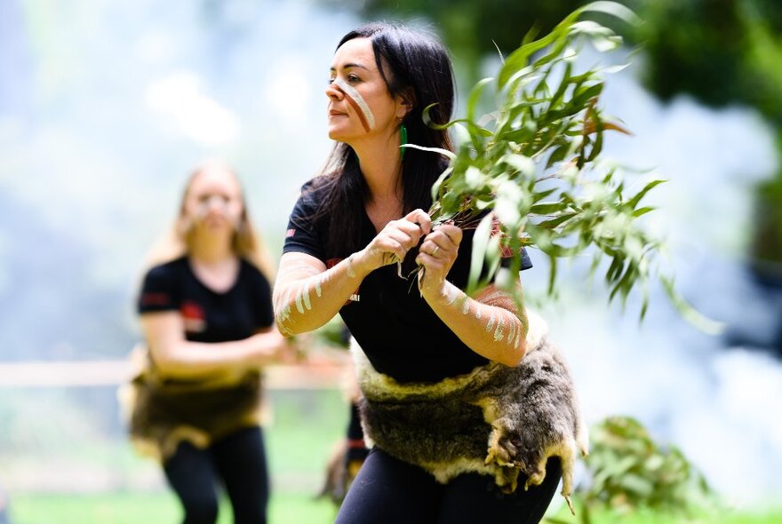 An Ingigenous woman holding up branches of a gum tree in a ceremony.