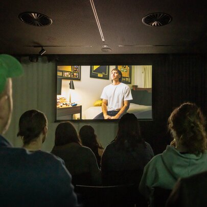 A small room with people watching a film on a small screen. 