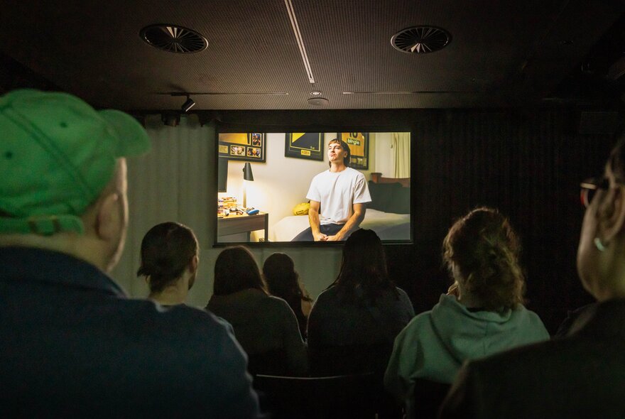 A small room with people watching a film on a small screen. 