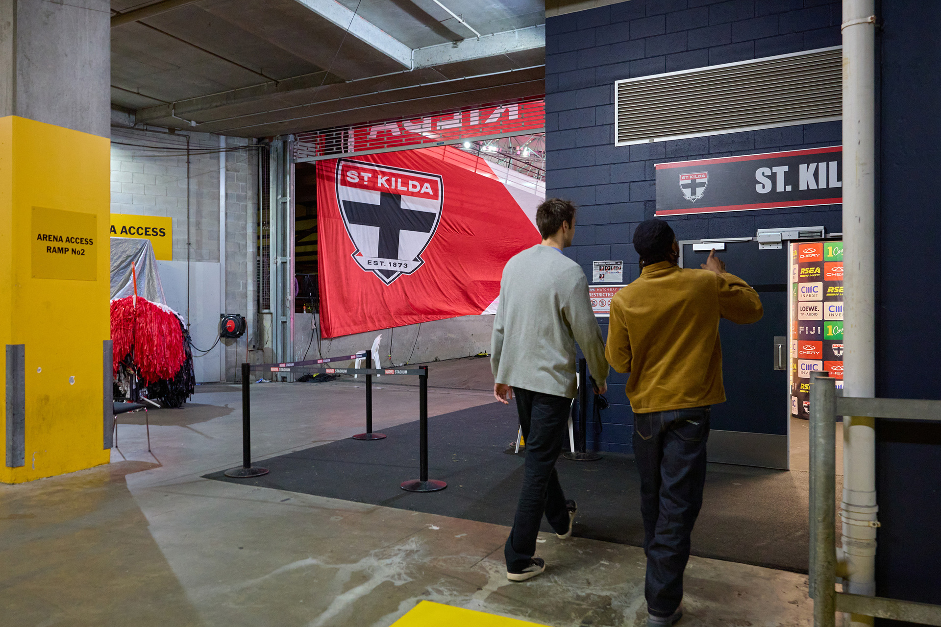 Two people are on a tour of Marvel Stadium they are walking into the locker rooms of the St Kilda football club