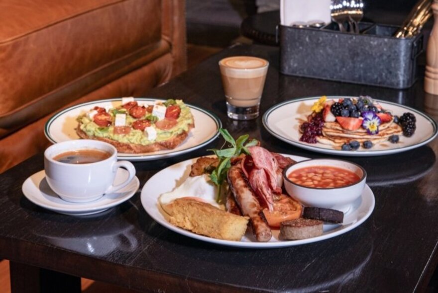 Dishes of food, cooked breakfast and salad, next to a cup of tea and glass of coffee.