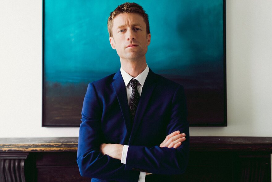 Man wearing a suit and tie, standing with his arms folded.