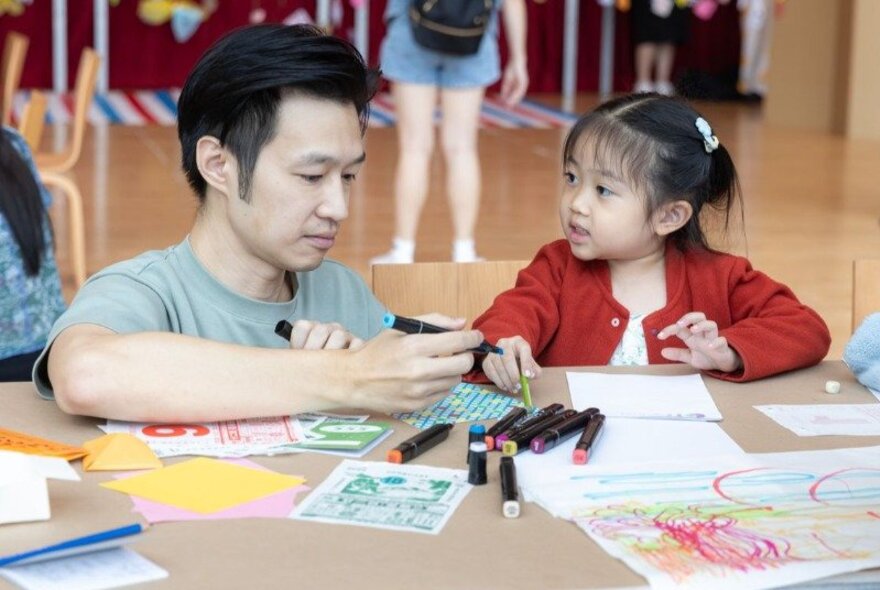 An older Asian man and a young Asian child, drawing together in a workshop environment.