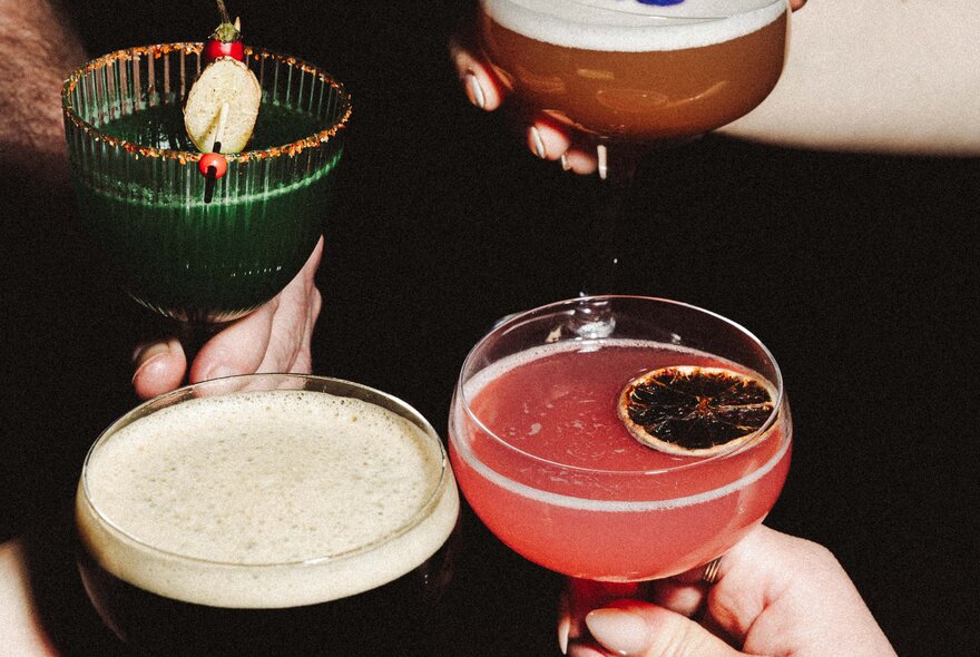 Four different cocktails being help by hands. 