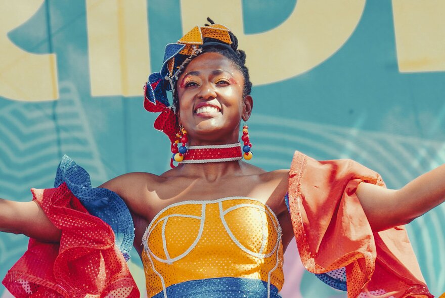 A smiling woman wearing a colourful dress with puffy sleeves and a matching headpiece, and dangling earrings.