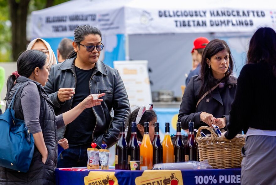 People sampling fare at an outdoor market stall.