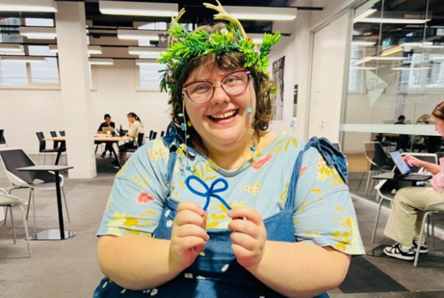 Woman wearing a green crown, holding a bow, in a library setting.