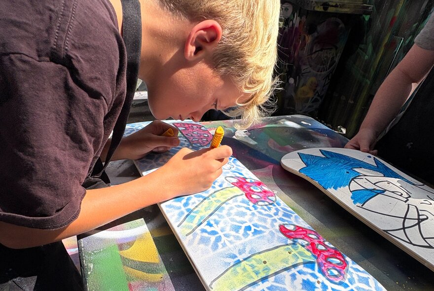 Child adding details to artwork on the back of a skateboard deck.