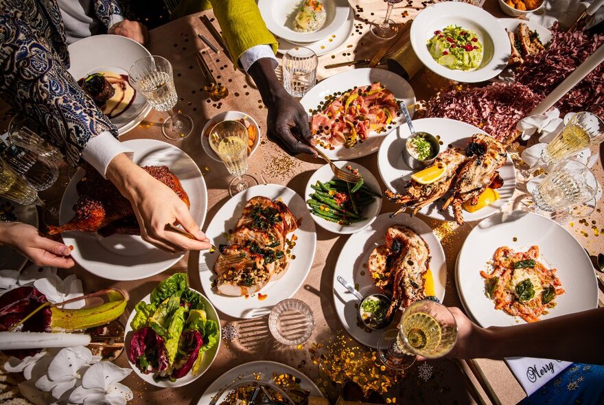 People's hands reaching in to select food from an array of shared platters on a table.