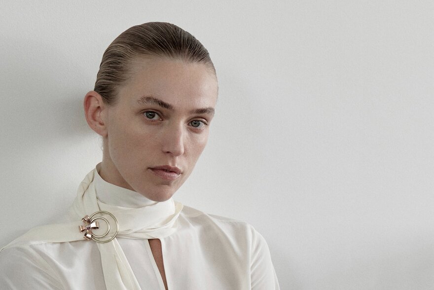 Model wearing an antique gold brooch and white outfit with scarf.