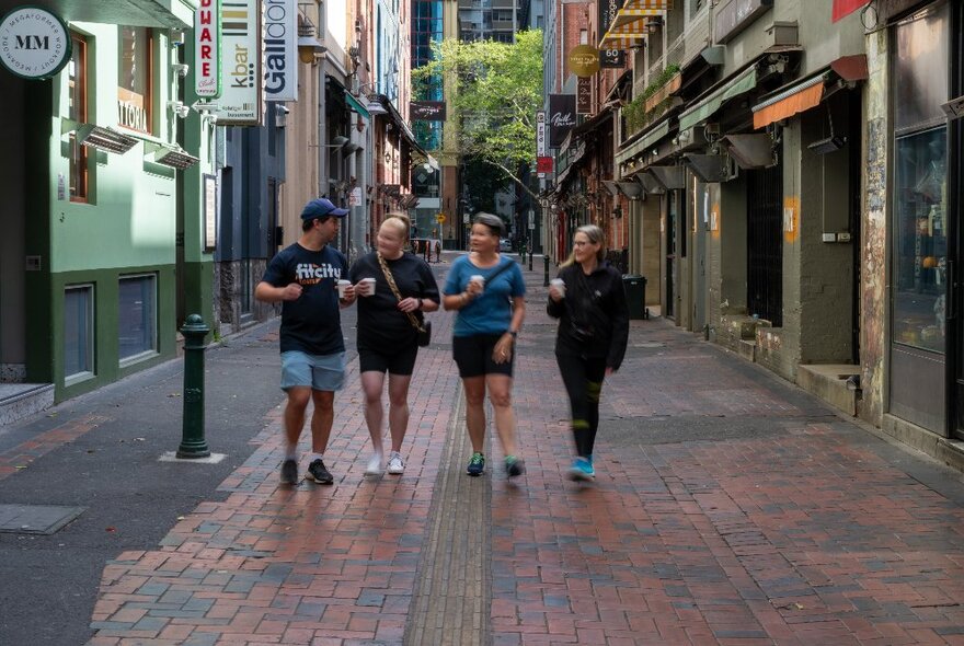 Three people on a walking tour with a Fit City tour guide, each carrying a takeaway coffee.