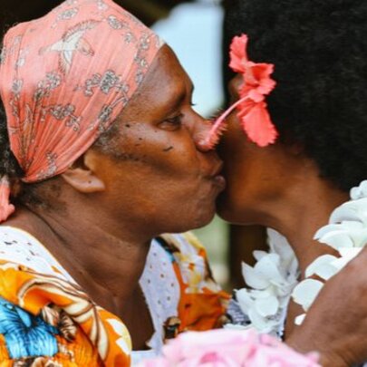 Two First Nations women greeting each other with a kiss on the cheek.