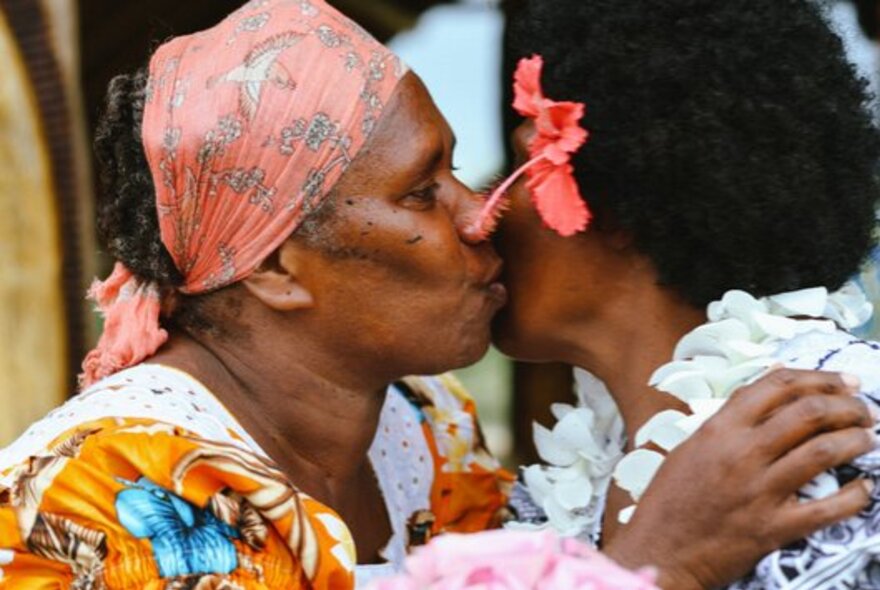 Two First Nations women greeting each other with a kiss on the cheek.