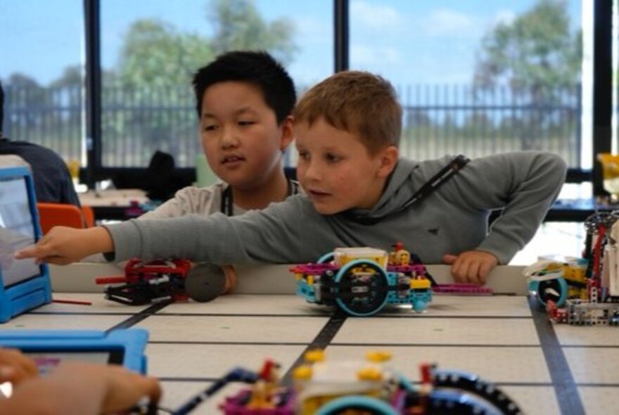 Two children engaging in a LEGO robotics workshop, using digital devices and LEGO bricks to build robotic models.