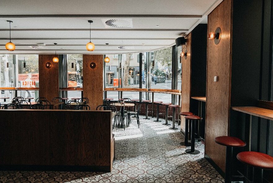 Interior of Rustica cafe with windows looking onto the city street, high stools under high bench tables, and patterned tiled floor and hanging lights.