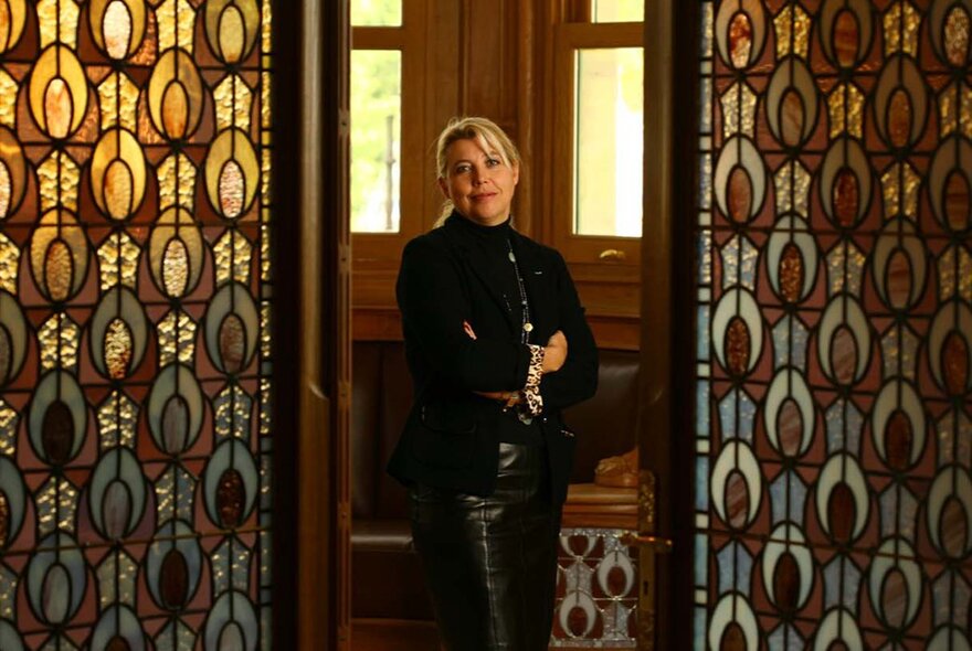 A stylish woman in black, standing between two stained glass panels, the light coming from behind her.