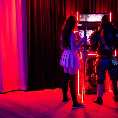 Two figures wearing gaming costumes standing at an illuminated games machine.