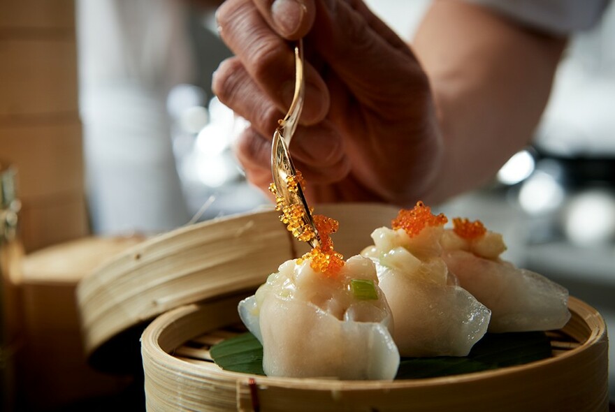 Someone spooning orange roe on to the top of some dumplings in a steamer.