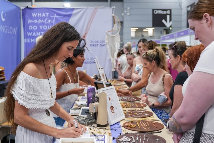 People looking at products on display at a booth at the MindBodySpirit Festival, and engaging with the stall holders.