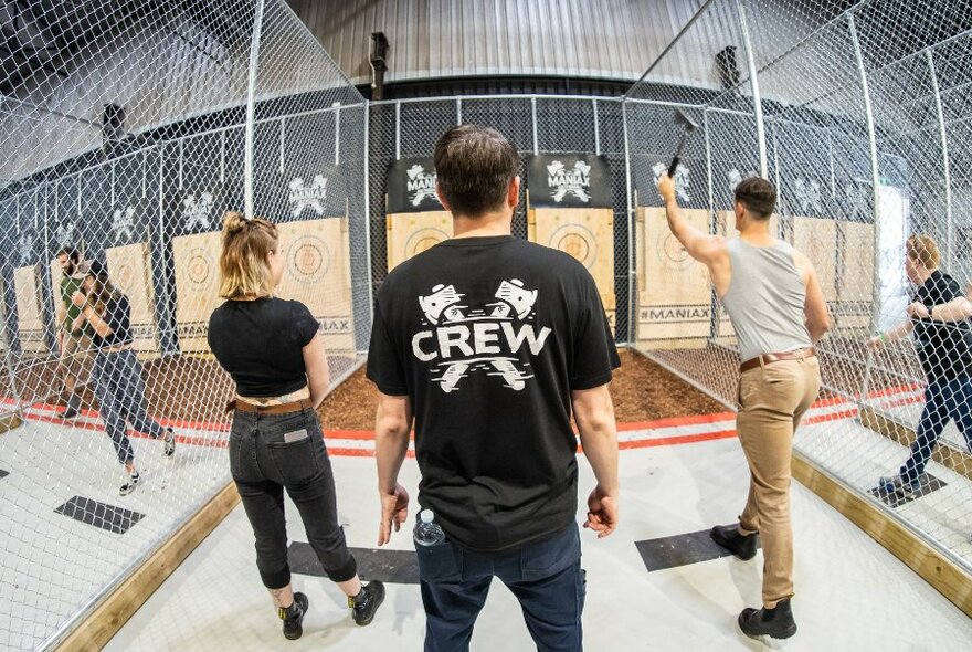 Staff and customers throwing axes in a wire-fenced venue.