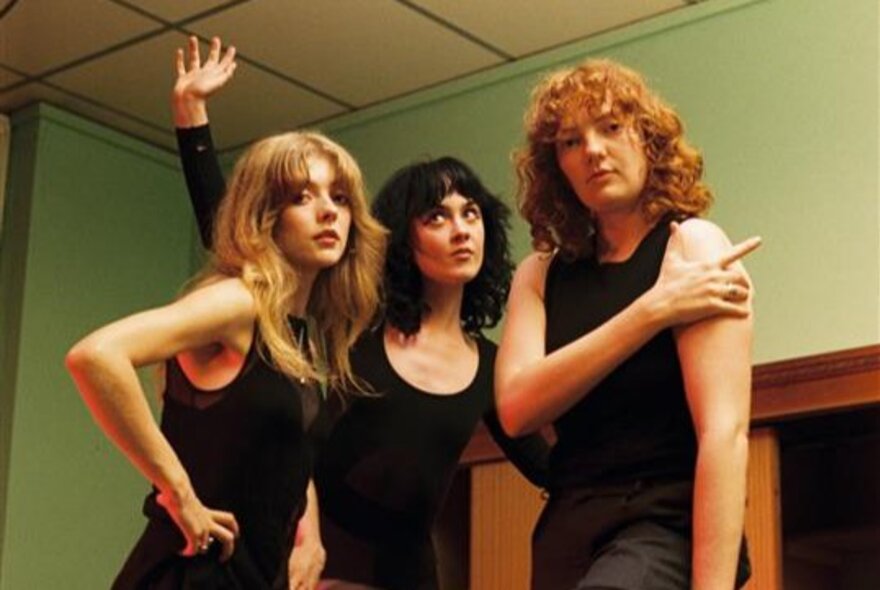 Musical trio wearing black tops in a room with green walls.