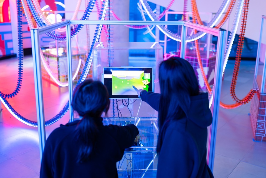 Two young people seen from behind, pointing at a display screen, at an interactive exhibition at the Science Gallery.