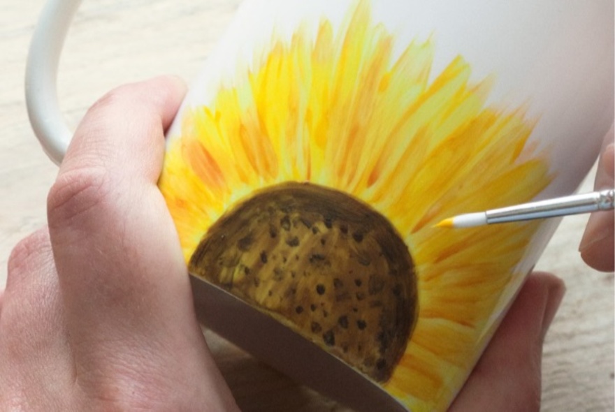 Hand painting a sunflower on a cup.