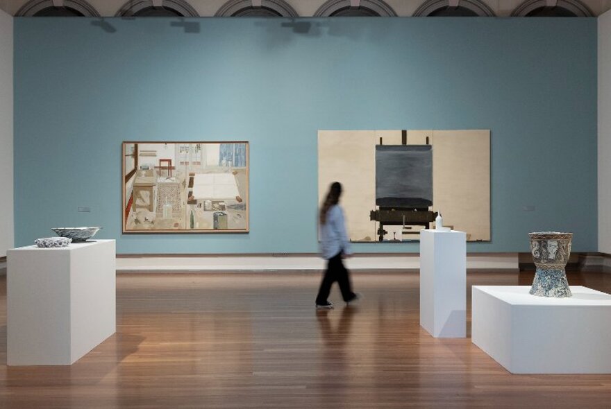 A gallery space with timber floors and a pale blue wall, with a selection of wall art and sculpture on display.