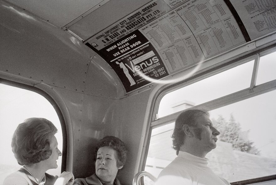 Old black-and-white photo of people seated on a bus, two women chatting, a man looking straight ahead.