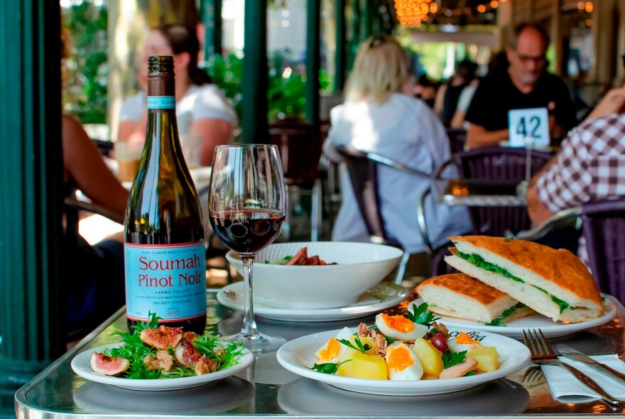 Outdoor cafe table with wine and plates of food including panini and salads.