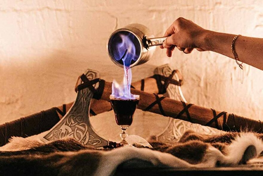 Flaming wine being poured into a glass surrounded by Viking axes