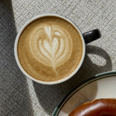 Cup of coffee with heart design next to a bagel on a plate.