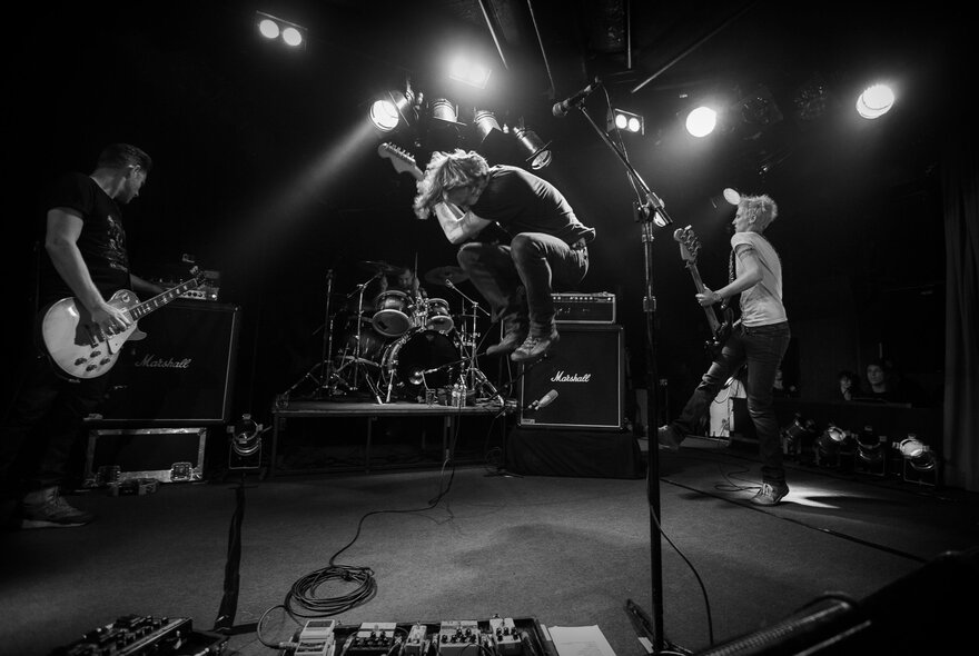 A black and white still from the documentary film 'Jebediah: Are We OK?' shows the band playing live and energetically on stage.