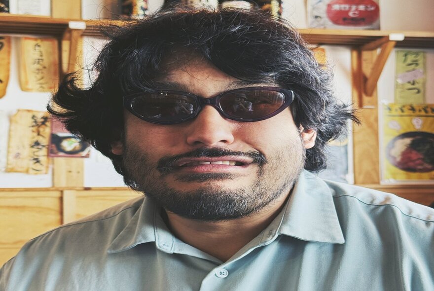 Stretched image of the comedian David Correos with dark hair and wearing dark sunglasses.