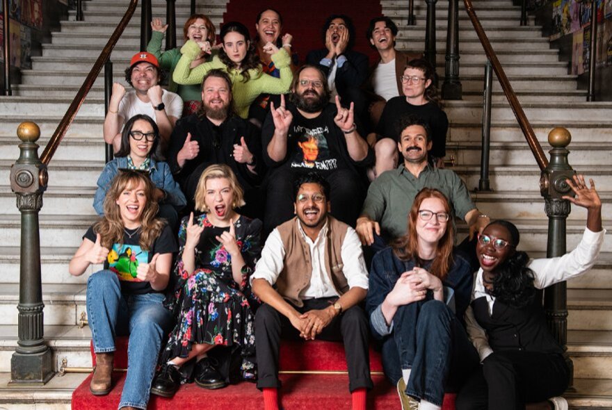 A large group of smiling people sitting on the central marble staircase at the Melbourne Town Hall.