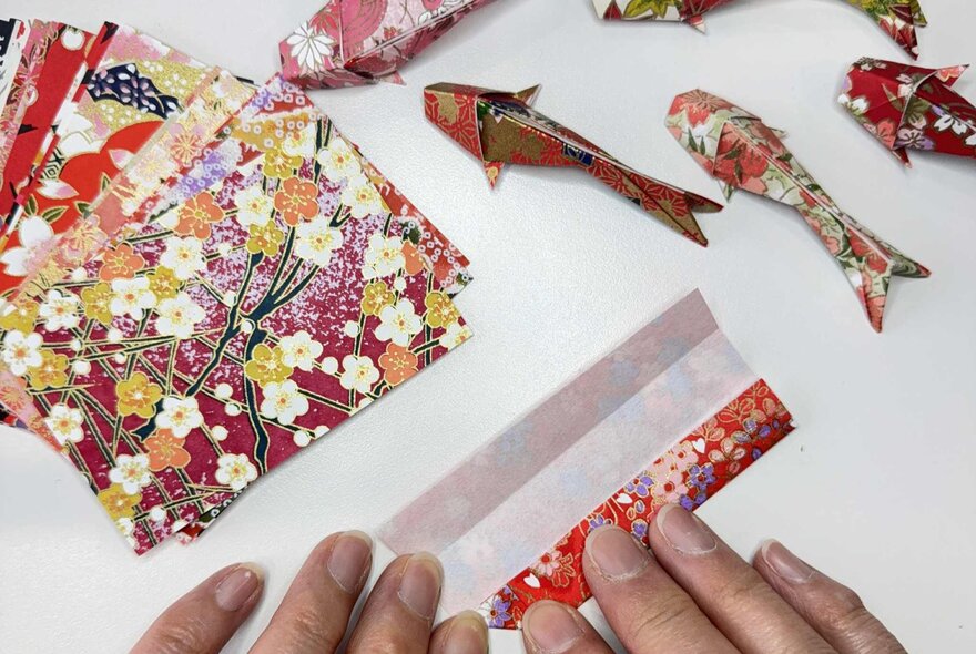 Hands folding Japanese craft paper and making origami koi fish.