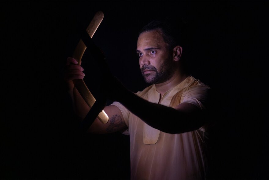 A man in profile view against a dark background, holding a soft light.