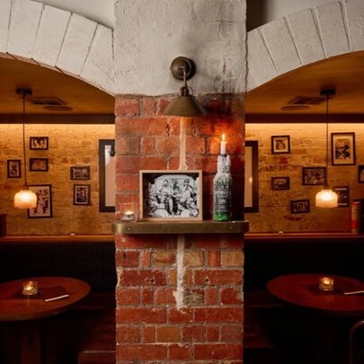 Two moodily-lit private booths at a venue, with a brick wall separating them and brick archways over the entrances to each booth.