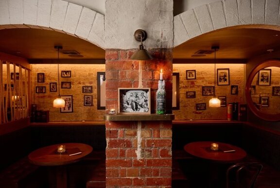 Two moodily-lit private booths at a venue, with a brick wall separating them and brick archways over the entrances to each booth.