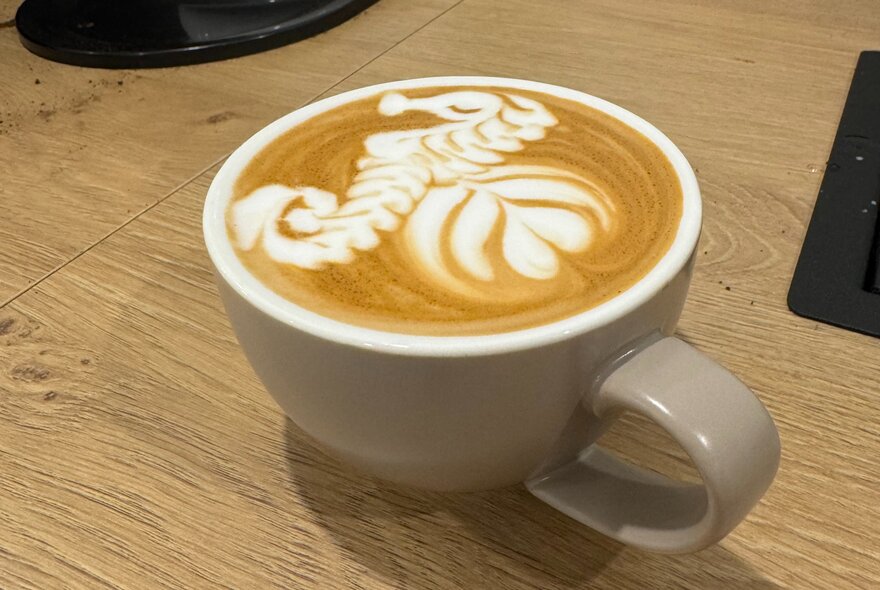 A cappuccino in a small cream-coloured mug with floral latte art in the milk.