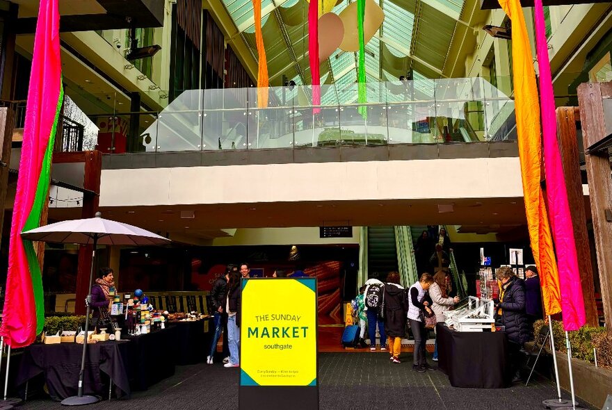 The entrance to the Sunday markets at Southgate, showing market stalls and a large yellow sandwich board.