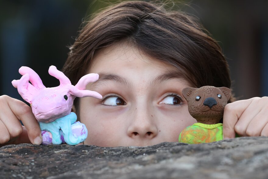 A child holding two polymer clay animal sculptures, hiding behind a wall.