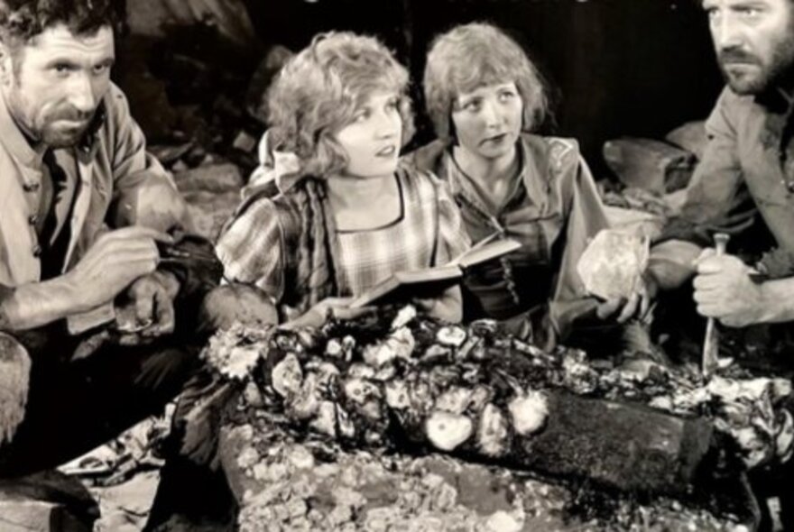 Still from the Australian silent movie For the Term of His Natural Life, two men and two women seated by logs.