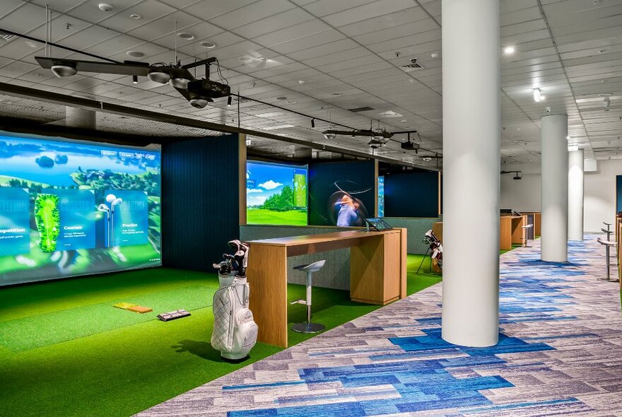 Indoor simulated golf course bays with course projections on big screens, and a person swinging a golf club.