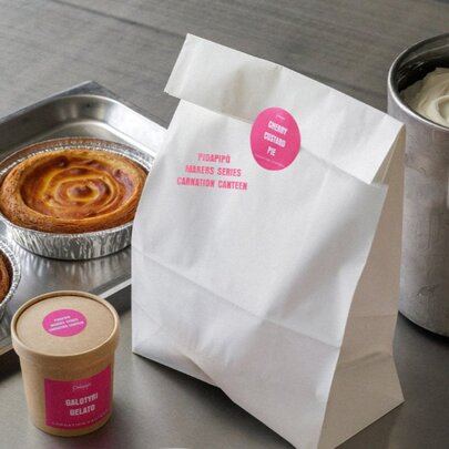 Two cherry pies on a tray, a takeaway container of gelato, and a sealed white paper bag.