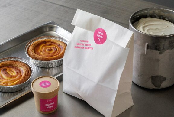 Two cherry pies on a tray, a takeaway container of gelato, and a sealed white paper bag.