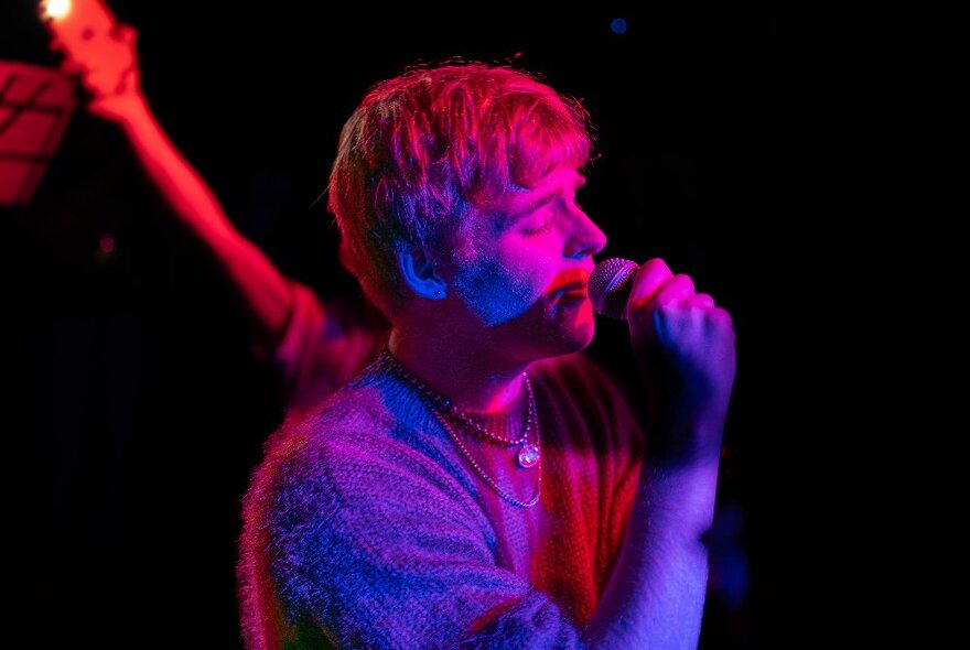 Singer performing with microphone under blue and red lights in a dark club.